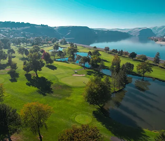 Aerial view of fairways and ponds beside a lake and hills