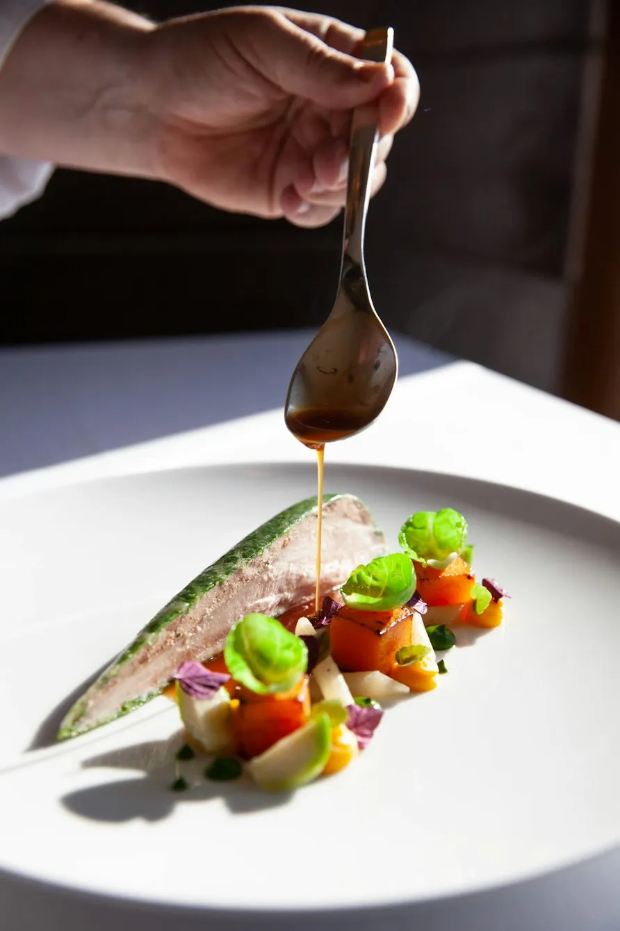 Chef spooning sauce over a plated fish dish