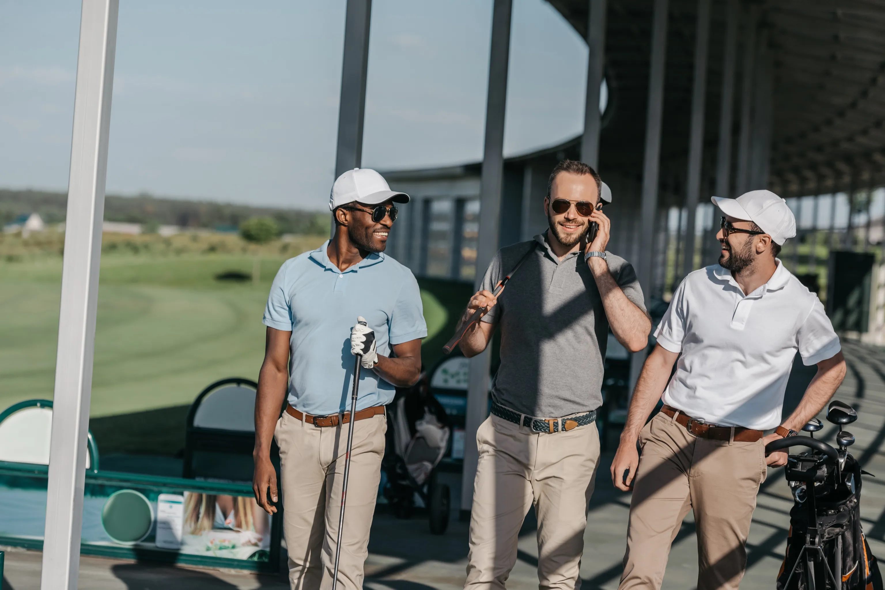 Three golfers laughing together at a driving range, one on the phone