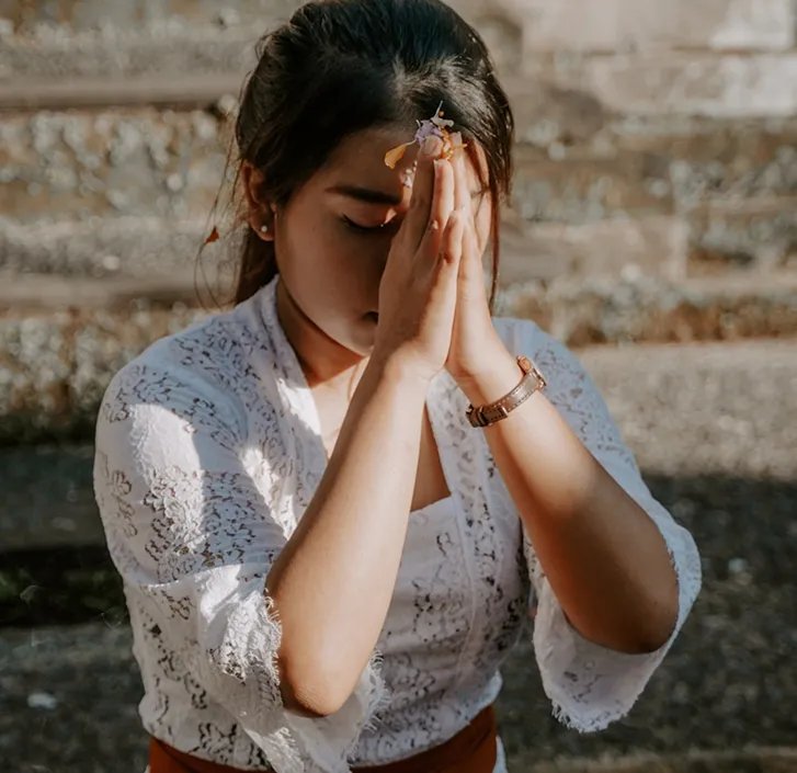 Balinese woman in a white lace kebaya praying with hands raised