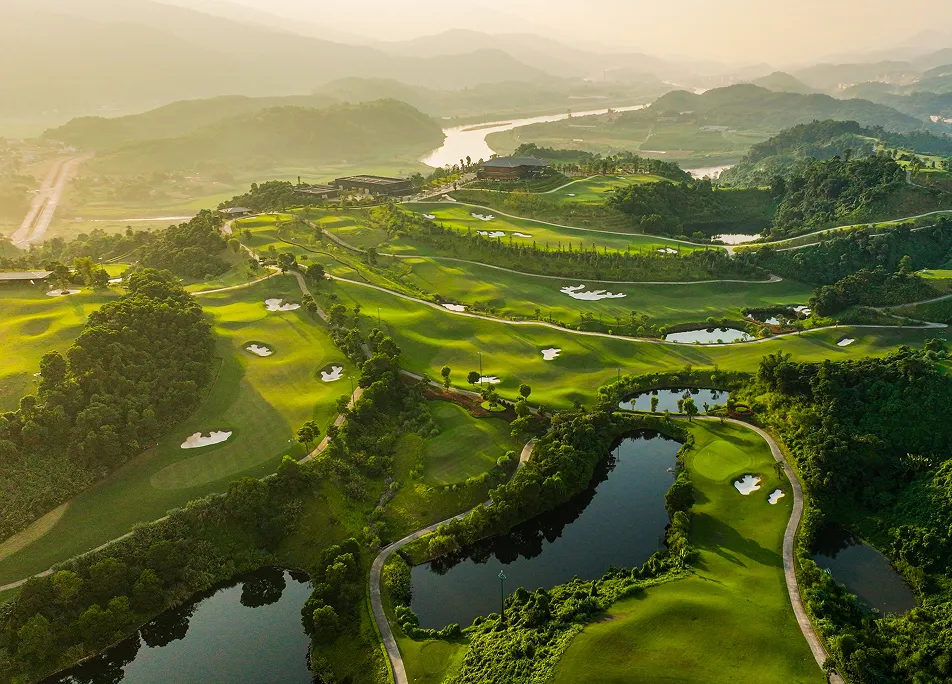 Aerial view of a hillside golf course with lakes and a river winding through misty valleys