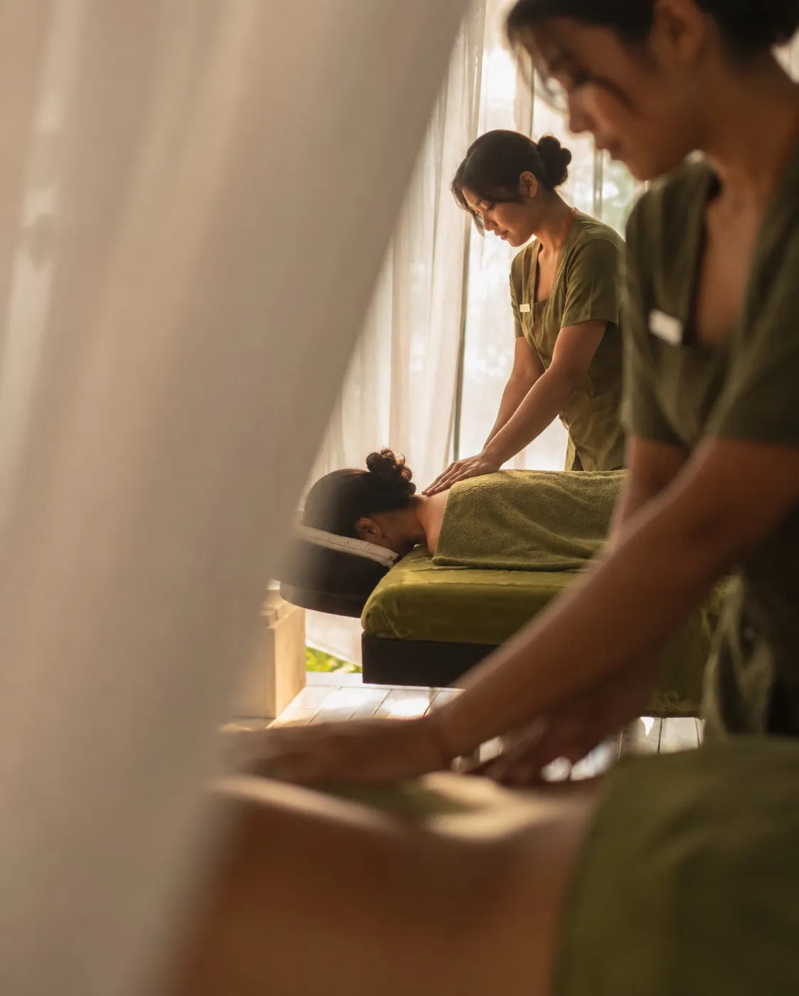 Therapists giving a massage beside a sheer curtain